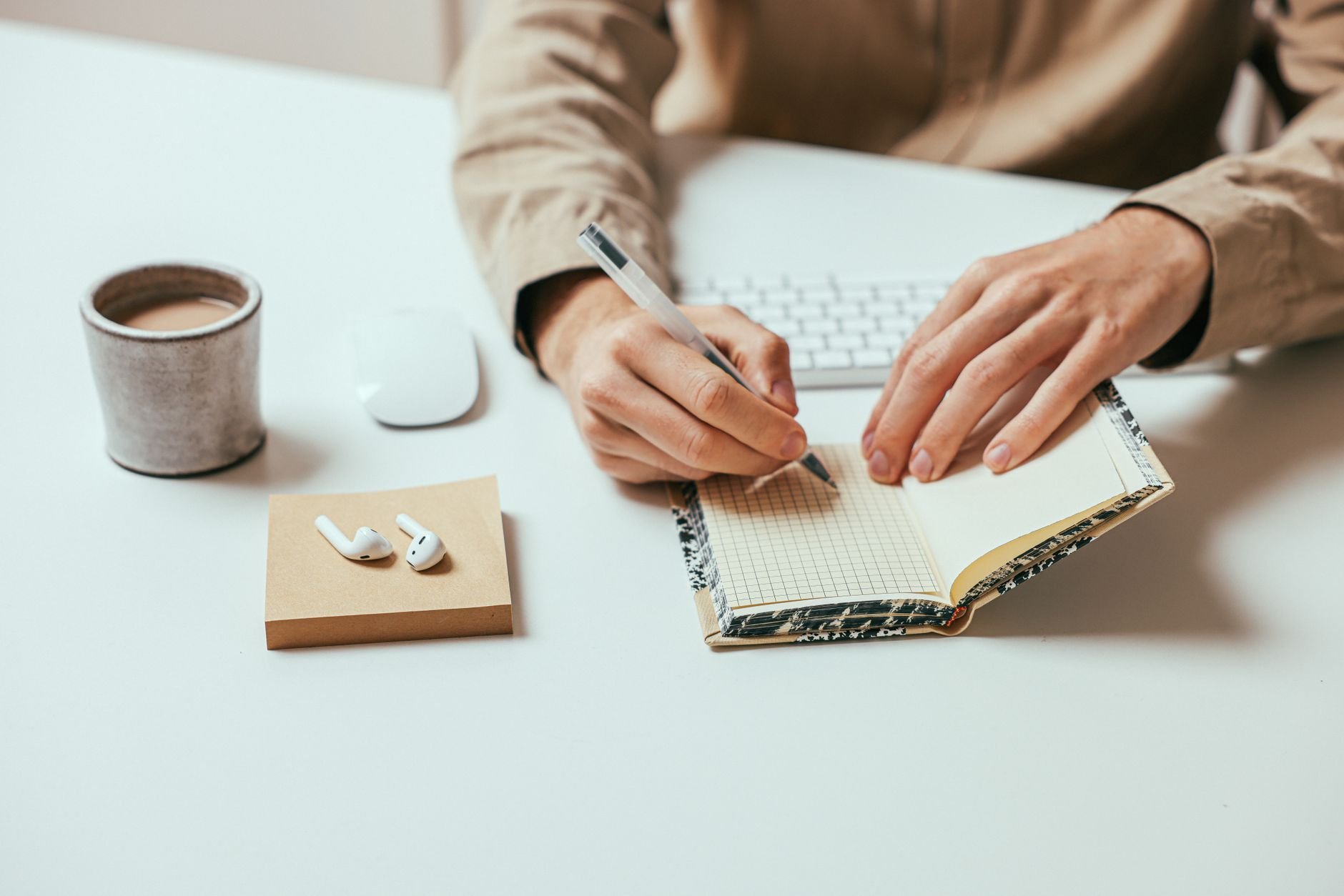 Person writing in a notebook on a desk with coffee nearby.